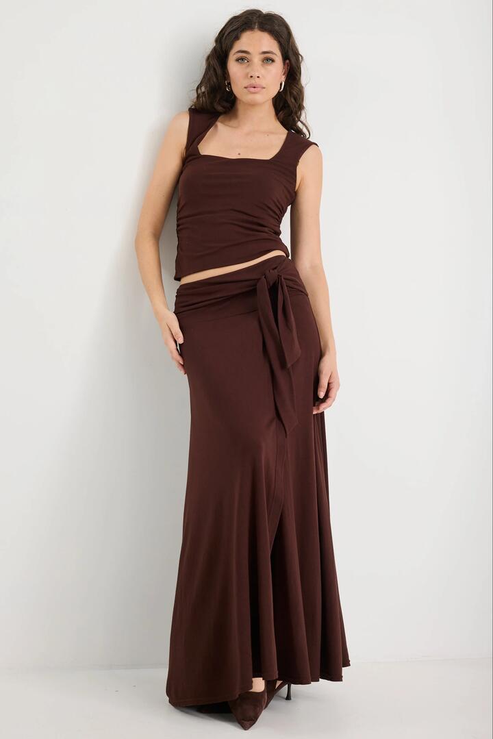 Image of a model wearing Skirts. Product name - Status Chocolate Jersey Knot Front Maxi Skirt in Chocolate colour by brand - Among the Brave