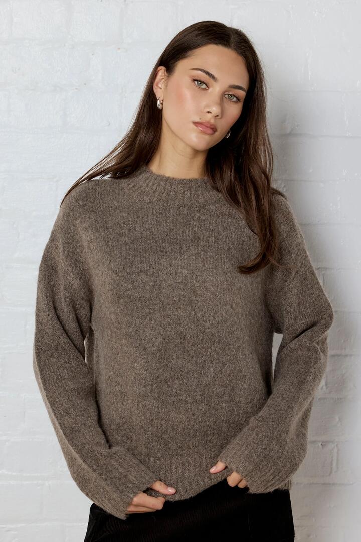 Image of a model wearing Outerwear. Product name - Cocoon Mocha Relaxed Knit Mock Neck Jumper in Mocha colour by brand - Among the Brave