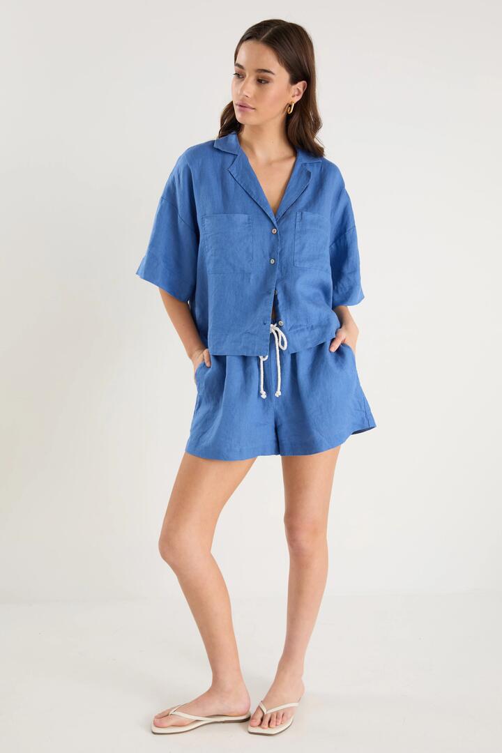 Image of a model wearing Shorts. Product name - Drift Cornflower Blue Linen Pull On Shorts in Cornflower Blue colour by brand - RE:UNION Label
