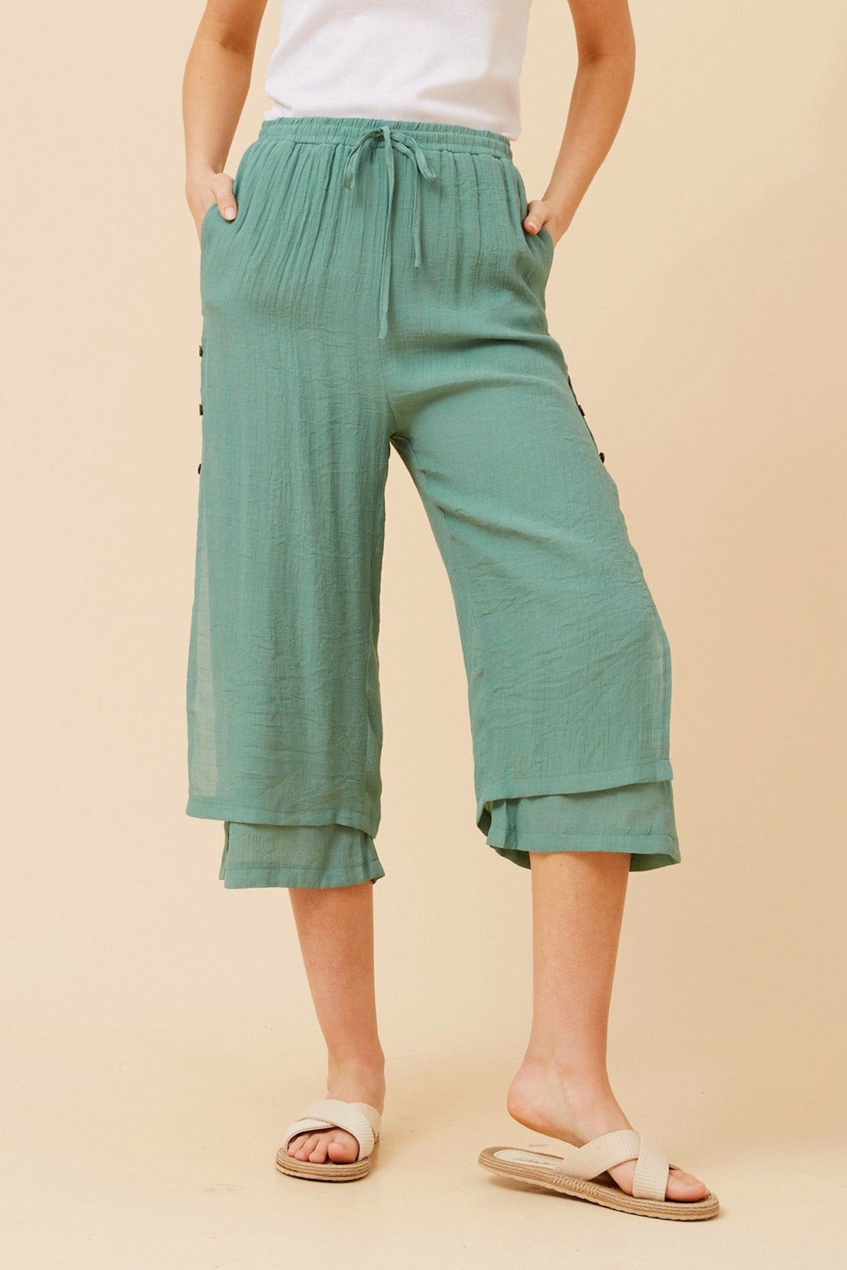 Image of a model wearing Pants. Product name - DAMIANA BUTTON DETAIL CULOTTES in Green Ash colour by brand - Caroline Morgan Australia