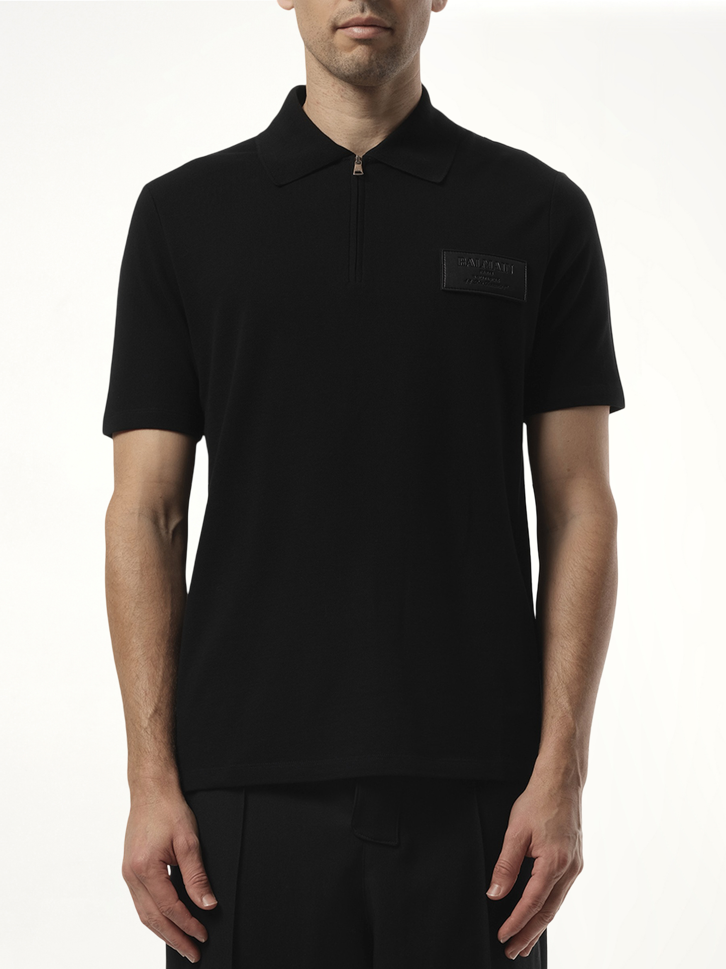 Image of a model wearing Tops. Productname: BALMAIN Small Leather Couture Label Zipped Polo in Black colour by brand - BALMAIN