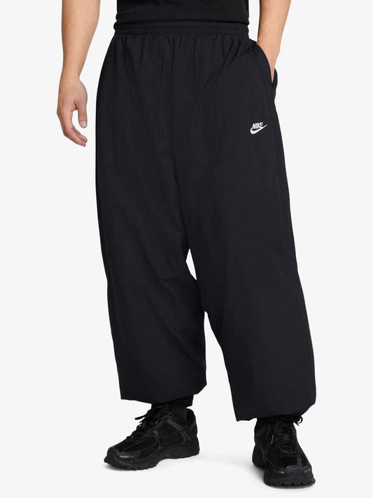 Image of a model wearing Pants. Productname: Nike Men's Club Oversized Woven Track Pants in Black/White colour by brand - Nike