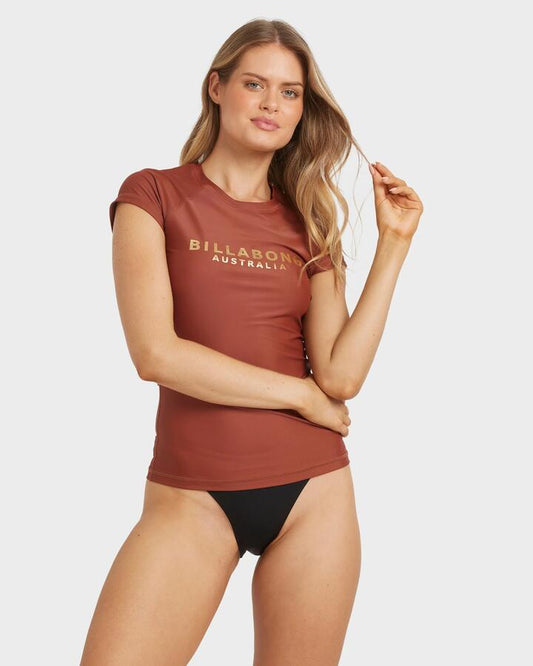 Image of a model wearing Tops. Product name - Billabong Womens Society Foil Short Sleeve Rash Vest Cowhide in Cowhide colour by brand - Billabong