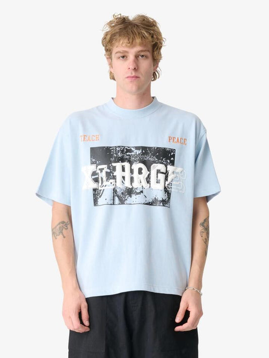 Image of a model wearing Tops. Productname: Xlarge Teach Peace Gorilla Fit Tee in Dusty Ice colour by brand - Xlarge
