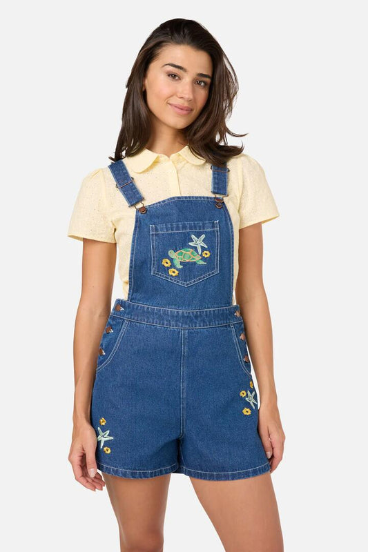 Image of a model wearing Pants. Product name - Turtle Embroidered Short Overall in Blue Denim colour by brand - Princess Highway