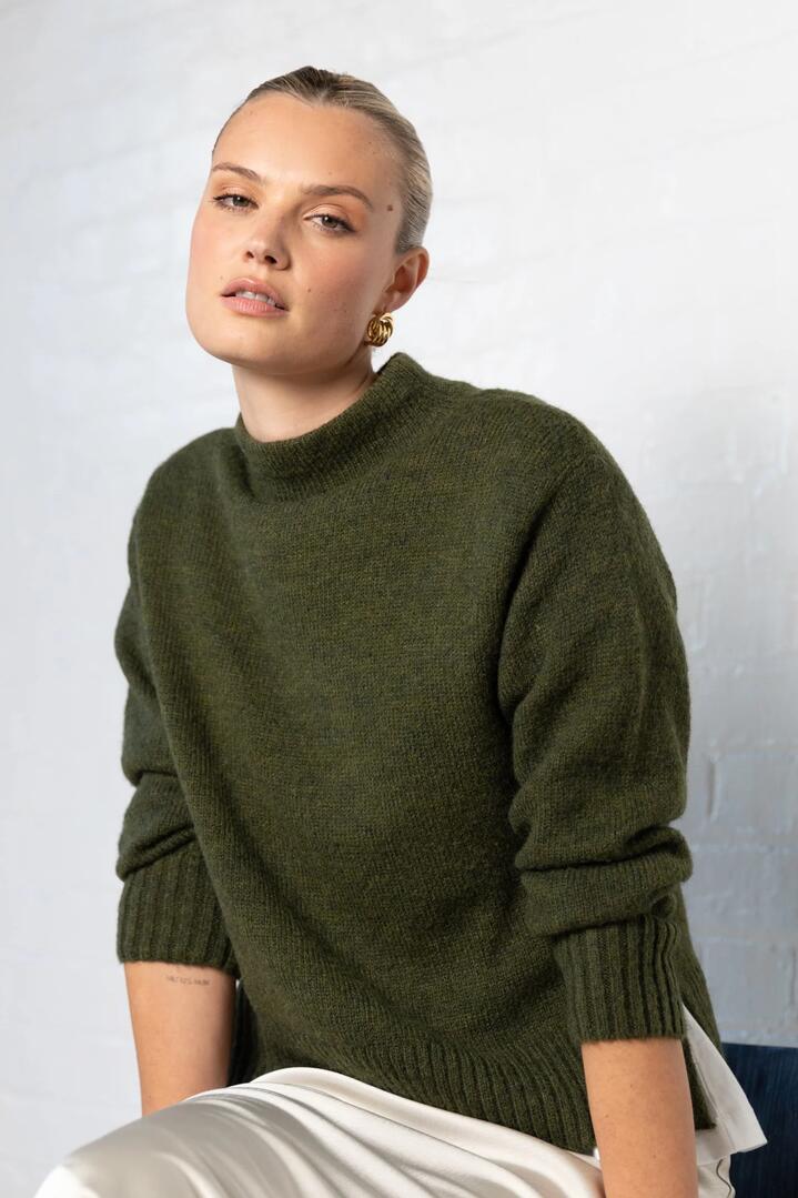 Image of a model wearing Outerwear. Product name - Huddle Khaki High Neck Knit Jumper in Khaki colour by brand - By Rosa.