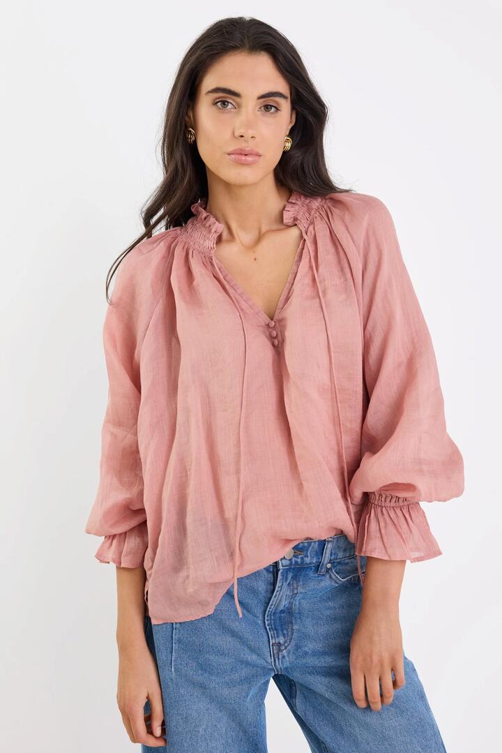 Image of a model wearing Tops. Product name - Odyssey Blush Shirred Neck Button Long Sleeve Top in Blush colour by brand - Among the Brave