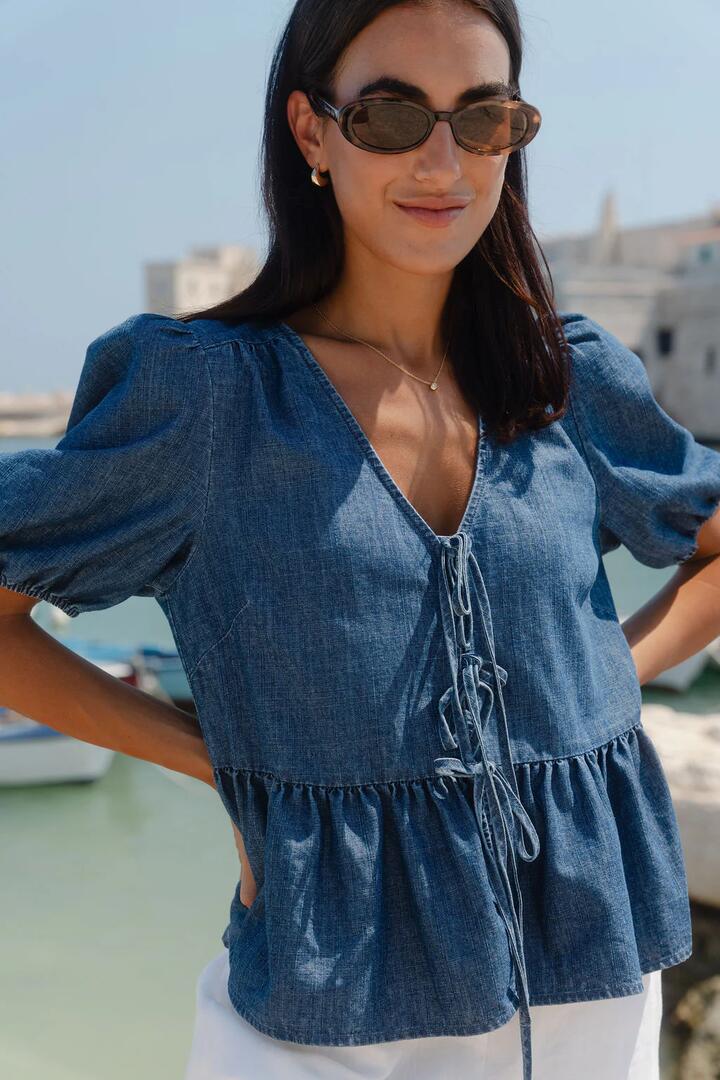 Image of a model wearing Tops. Product name - Restore Storm Blue Chambray Tie Front Peplum SS Top in Strom Blue Chambray colour by brand - Stories be Told