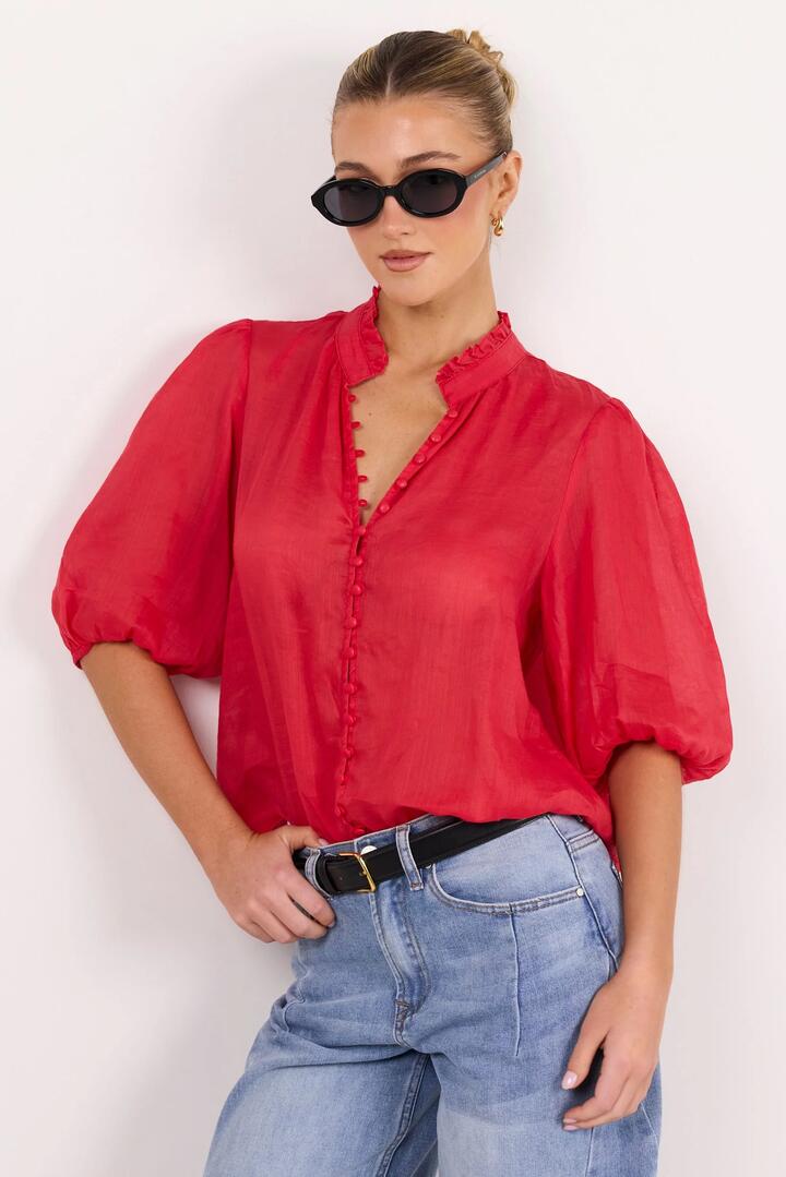Image of a model wearing Tops. Product name - Continuance Poppy Ramie High Neck Buttoned SS Top in Poppy colour by brand - Ivy + Jack