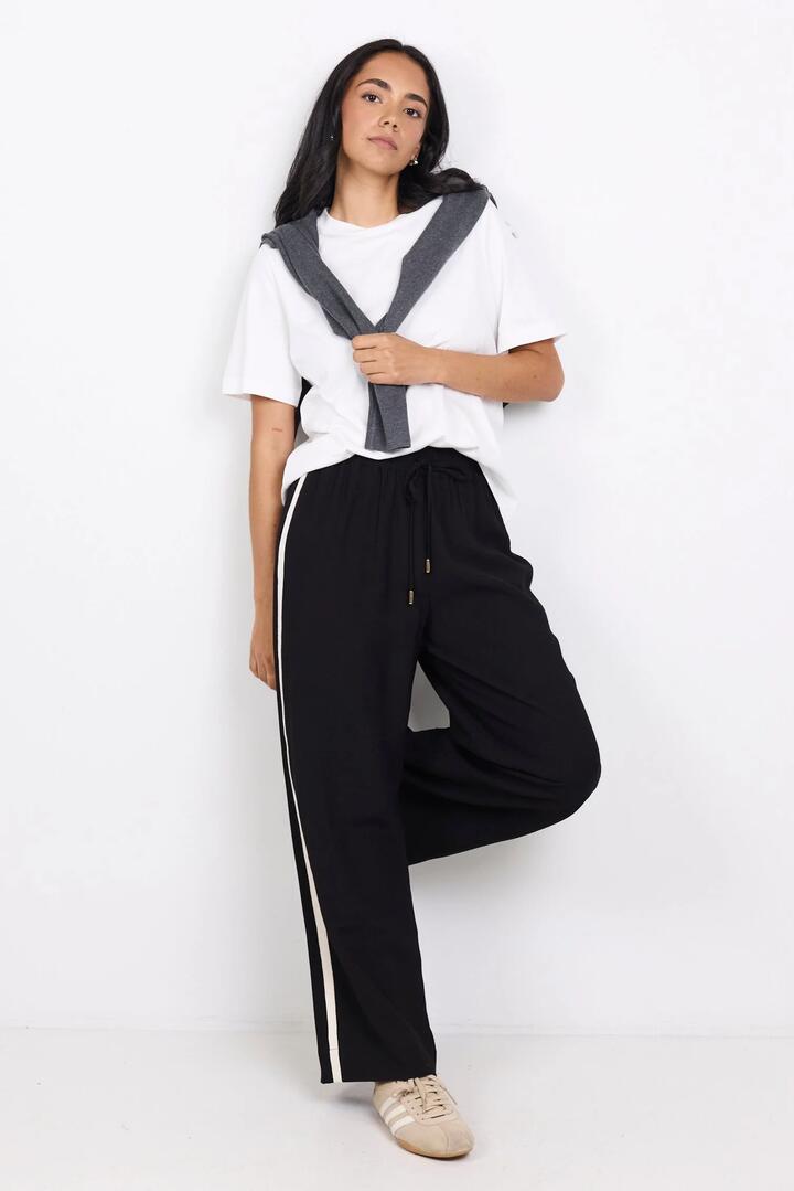 Image of a model wearing Pants. Product name - Townie Black Matte Petite Stripe Side Tape Wide Leg Pants in Black Matte colour by brand - Stories be Told