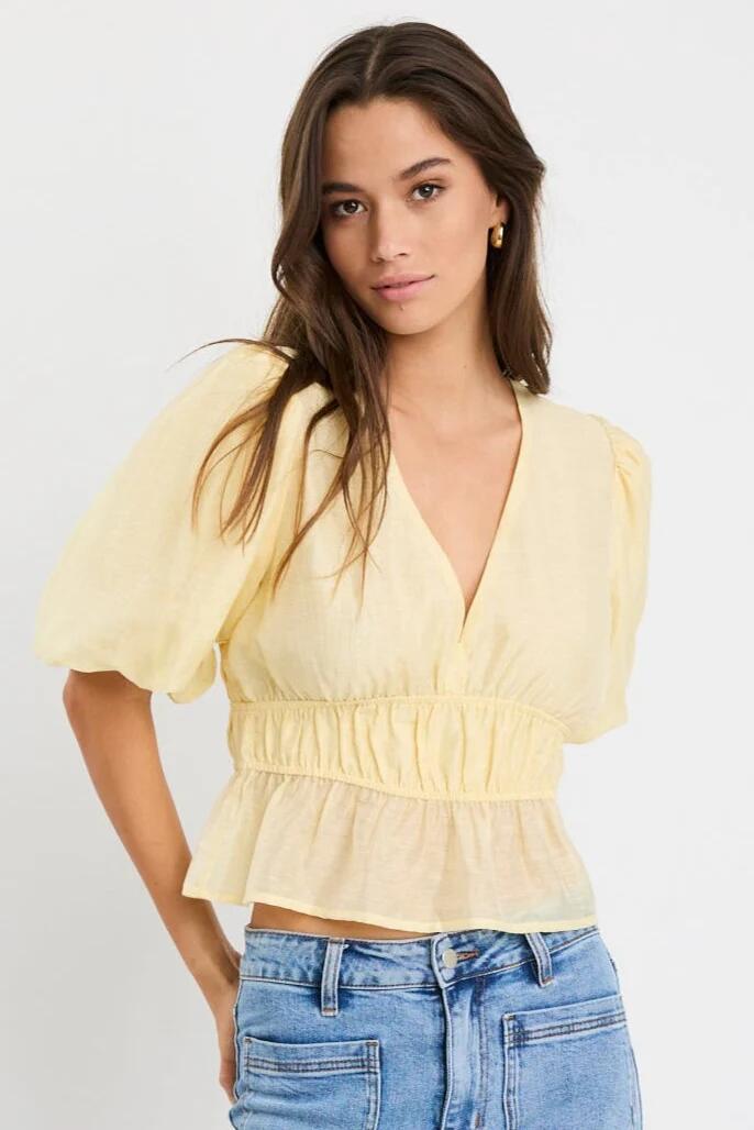 Image of a model wearing Tops. Product name - Vexing Butter Puff Sleeve V Top in Butter colour by brand - Georgia Zoe