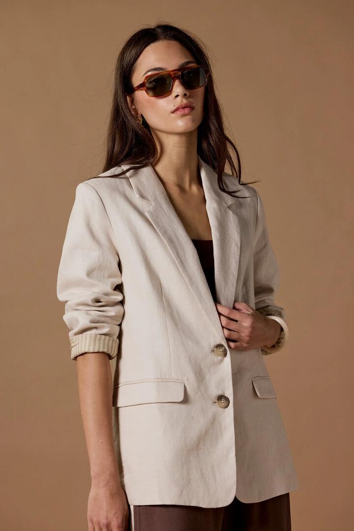 Image of a model wearing Outerwear. Product name - Pillar Cream Linen 2 Button Blazer in Cream Linen colour by brand - RE:UNION Label