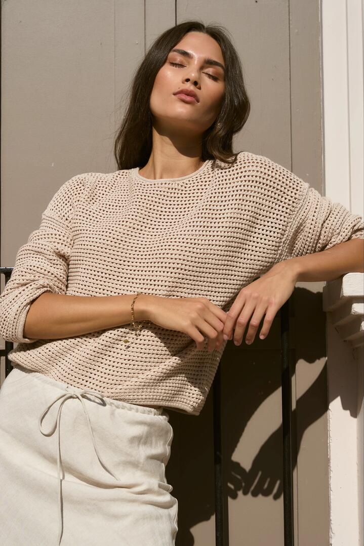 Image of a model wearing Outerwear. Product name - Dawn String Crochet Knit Jumper in String colour by brand - RE:UNION Label