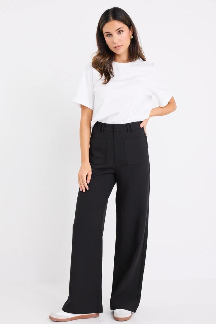 Image of a model wearing Pants. Product name - Zoey Black Tailored High Rise Wide Leg Pocket Pants in Black colour by brand - Among the Brave