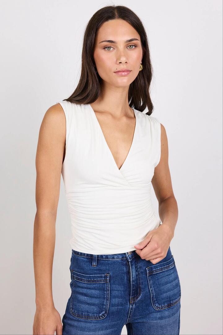Image of a model wearing Tops. Product name - Connect Ivory Jersey Cross Front Sleeveless Top in Ivory colour by brand - Stories be Told