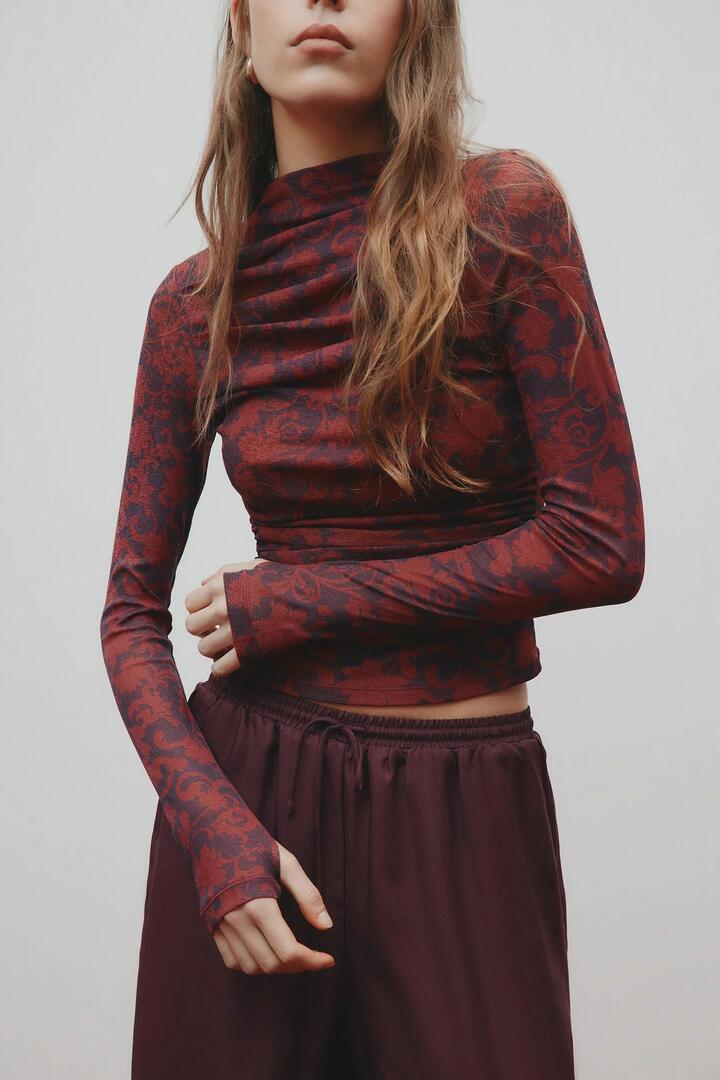 Image of a model wearing Tops. Product name - Clementine Berry Print Ruched Front LS Mesh Top in Red colour by brand - Nude Lucy
