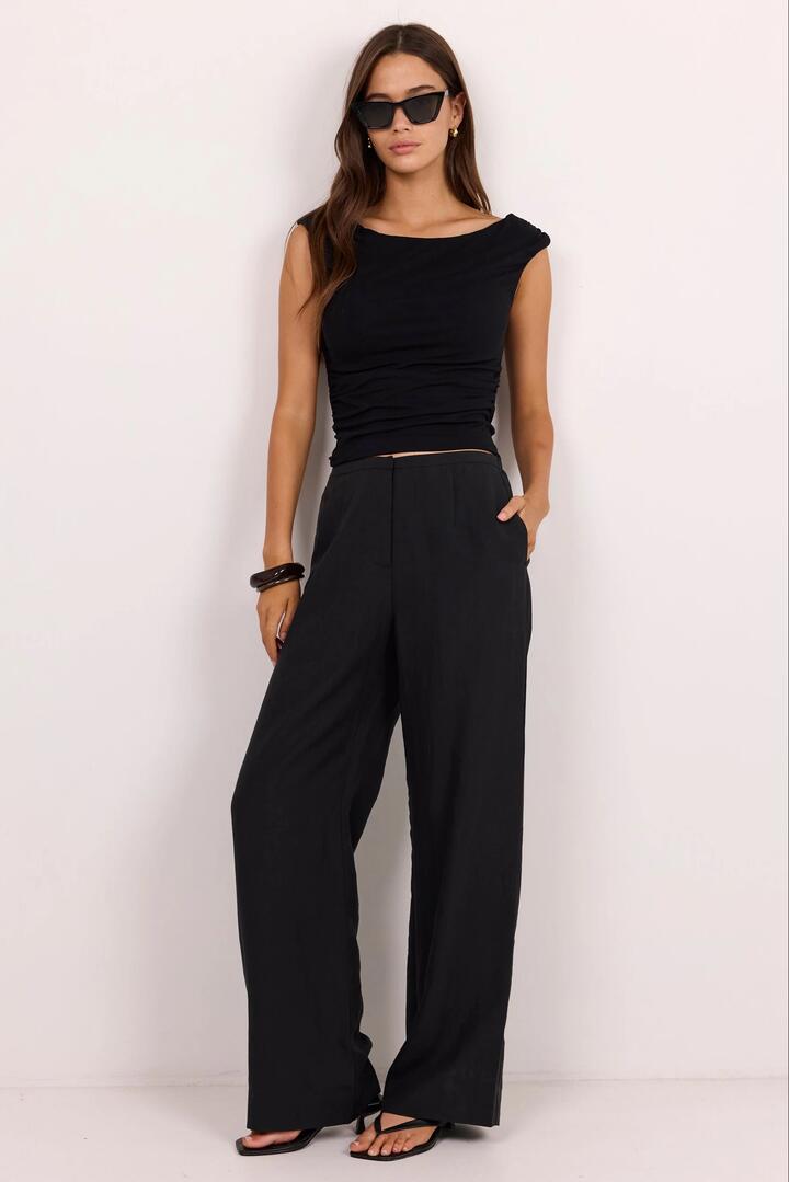 Image of a model wearing Pants. Product name - Charmed Soft Black Pleat Front Wide Leg Pants in Soft Black colour by brand - Stories be Told