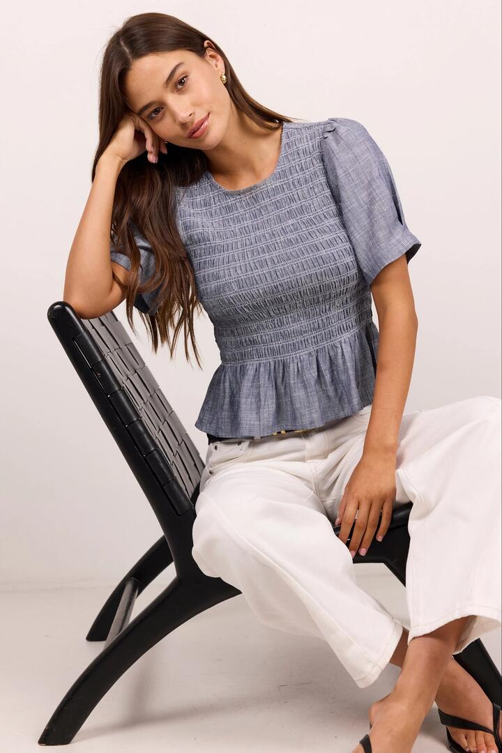 Image of a model wearing Tops. Product name - Starling Light Blue Chambray SS Shirred Bodice Top in Light Blue Chambray colour by brand - RE:UNION Label