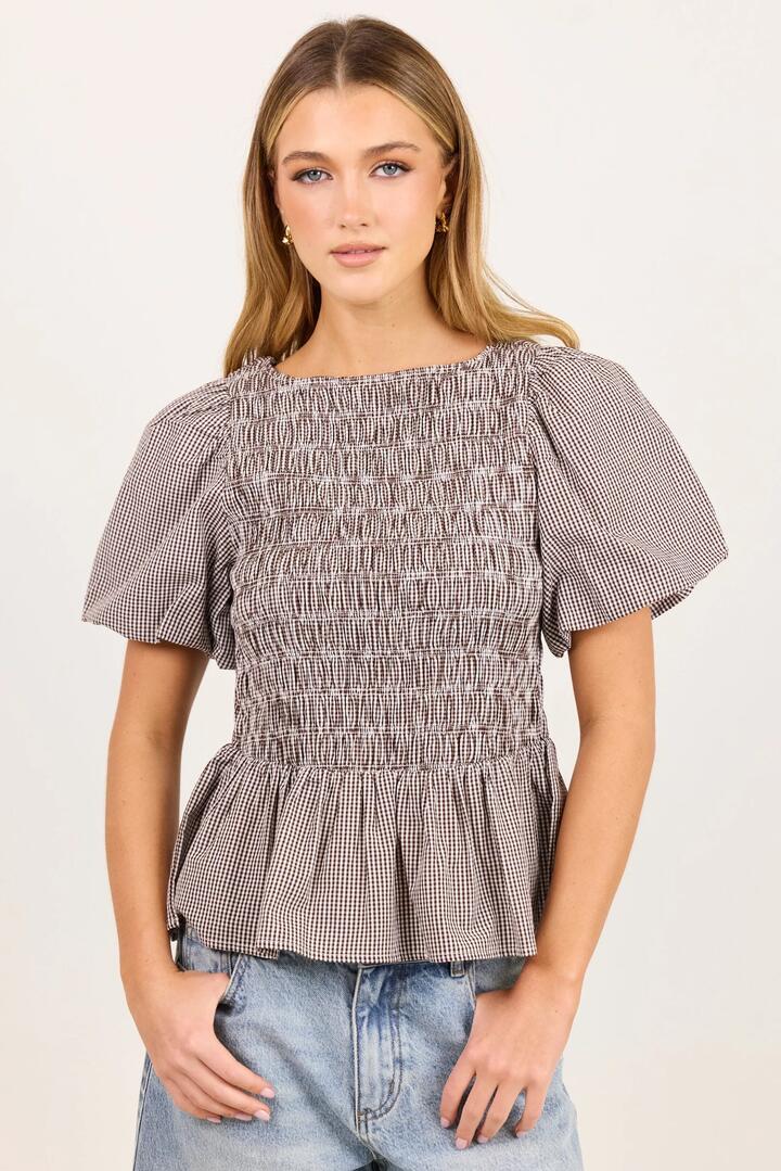 Image of a model wearing Tops. Product name - Artifact Chocolate Mini Gingham Shirred Bubble Sleeve Top in Chocolate Mini Gingham colour by brand - Stories be Told