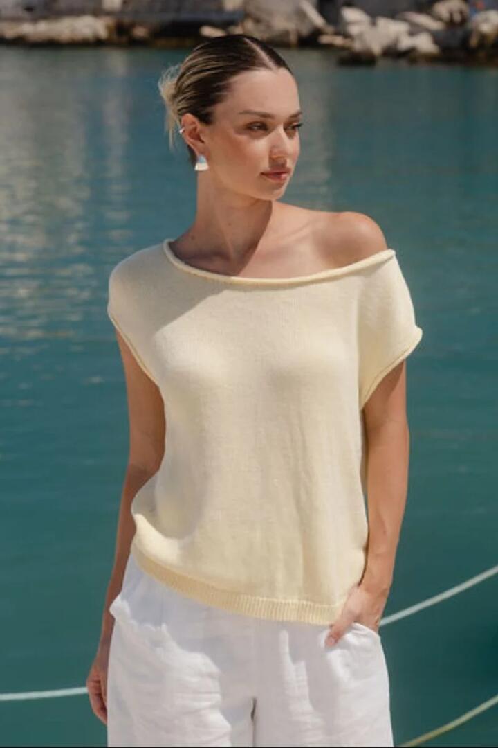 Image of a model wearing Outerwear. Product name - Fallow Butter Off Shoulder Sleeveless Knit Top in Butter colour by brand - RE:UNION Label