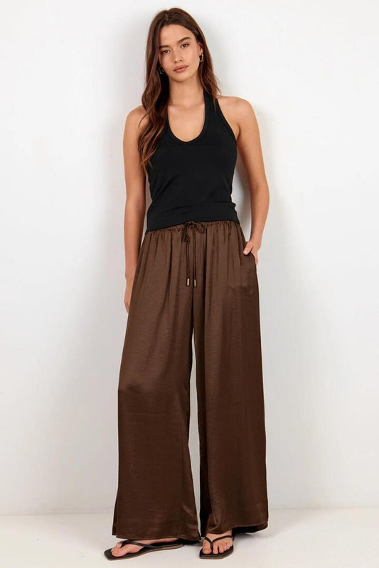 Image of a model wearing Pants. Product name - Canyon Chocolate Elastic Waist Satin Wide Leg Pants in Chocolate colour by brand - By Rosa.