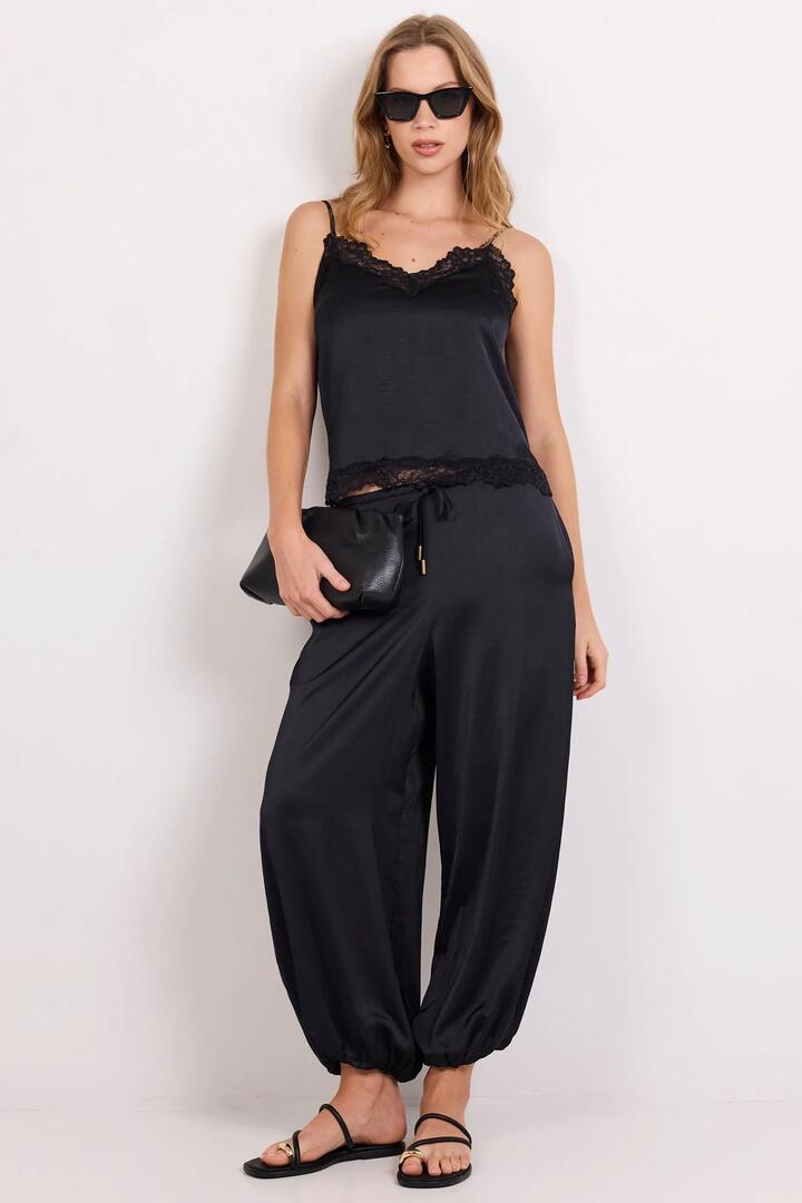 Image of a model wearing Pants. Product name - Fluidity Black Satin Balloon Pull On Pants in Black colour by brand - Stories be Told