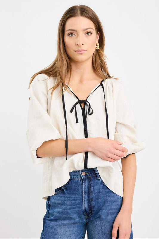 Image of a model wearing Tops. Product name - Subliminal Cream Black Trim Linen Relaxed LS Top in Cream colour by brand - RE:UNION Label