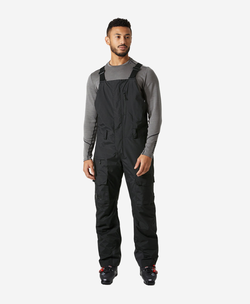 Image of a model wearing Pants. Product name - SOGN BIB CARGO PANT, Black in Black colour by brand - Helly Hansen
