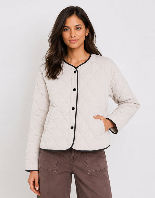 Image of a model wearing Outerwear. Product name - Apex Collarless Quilted Contrast Piping Puffer Jacket Bone in Bone colour by brand - Stories Be Told
