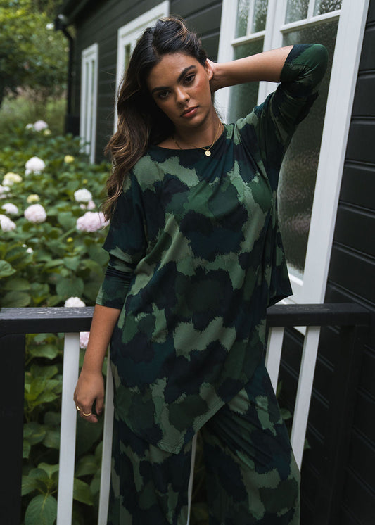 Image of a model wearing Tops. Product name - Susie Oversized Asymmetrical Bamboo Top Camouflage in Camouflage colour by brand - Lou Lou