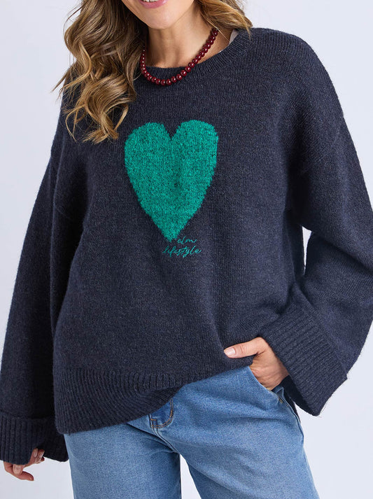 Image of a model wearing Outerwear. Product name - Elm Intersia Heart Knit in Navy A colour by brand - Elm
