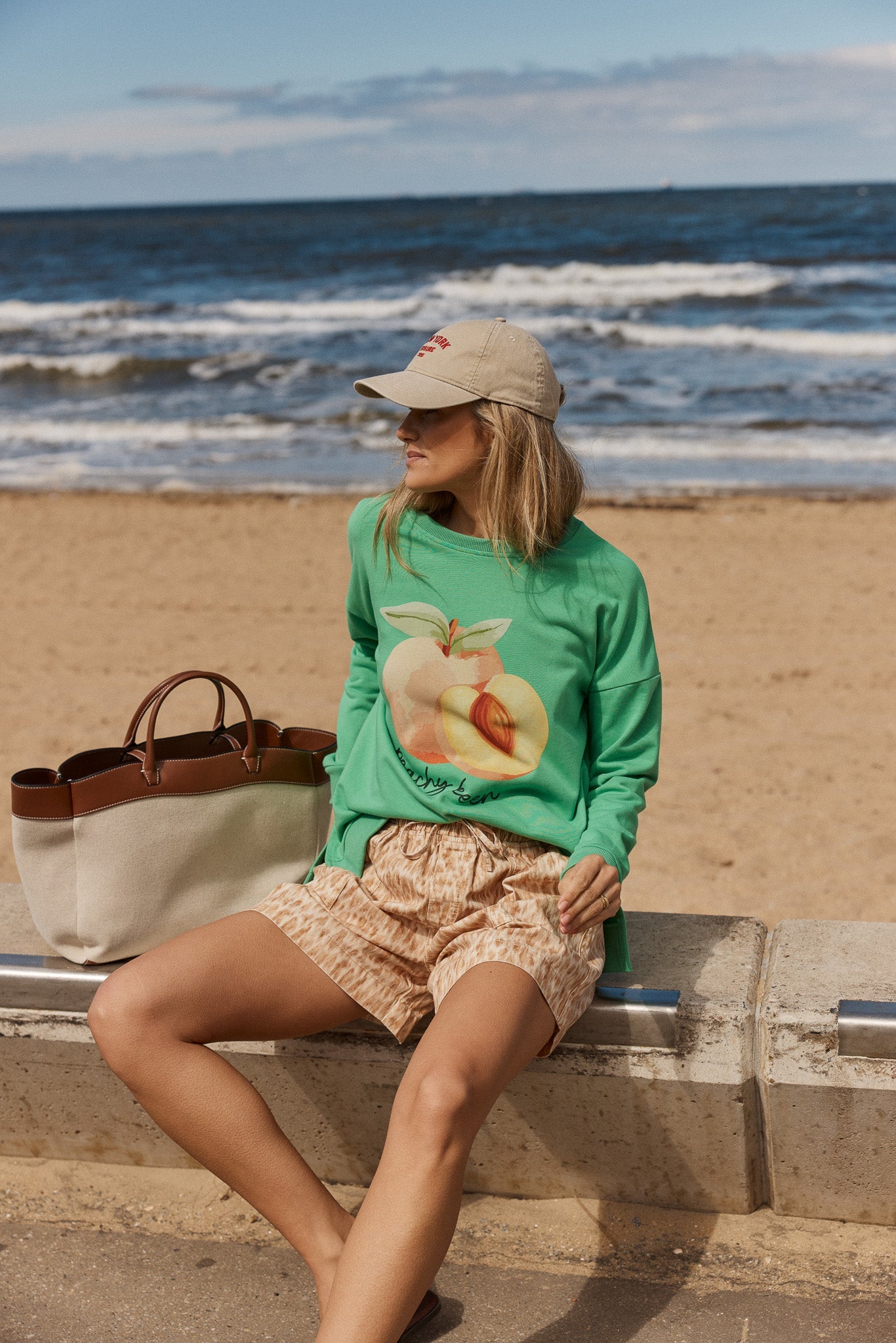 Image of a model wearing Outerwear. Product name - Palma Sweat in Peachy Keen Print colour by brand - Betty Basics