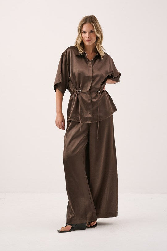 Image of a model wearing Pants. Product name - Aurora Satin Pant Chocolate in Chocolate colour by brand - Sass Clothing