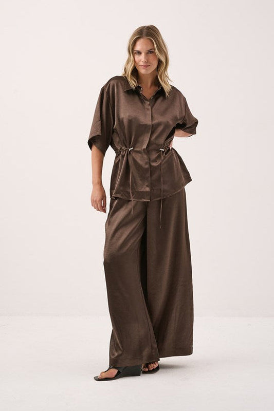Image of a model wearing Pants. Product name - Aurora Satin Pant Chocolate in Chocolate colour by brand - Sass Clothing