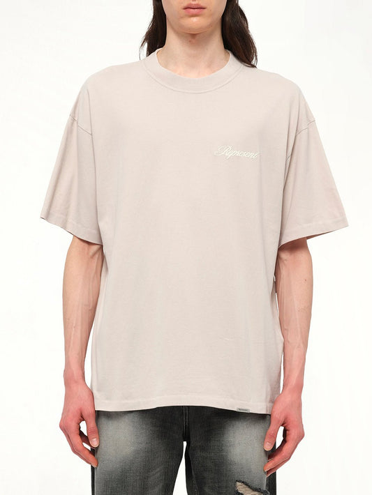 Image of a model wearing Tops. Productname: REPRESENT Script Logo T-Shirt in Concrete colour by brand - REPRESENT