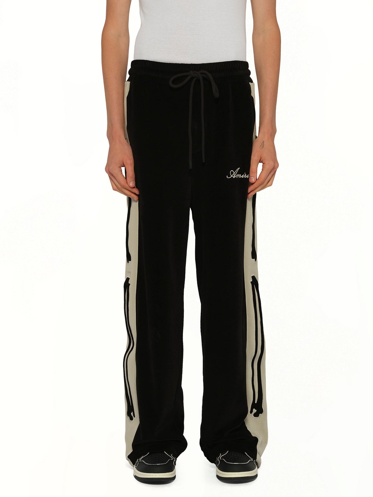 Image of a model wearing Pants. Product name - Bones Track Pant in Black colour by brand - AMIRI