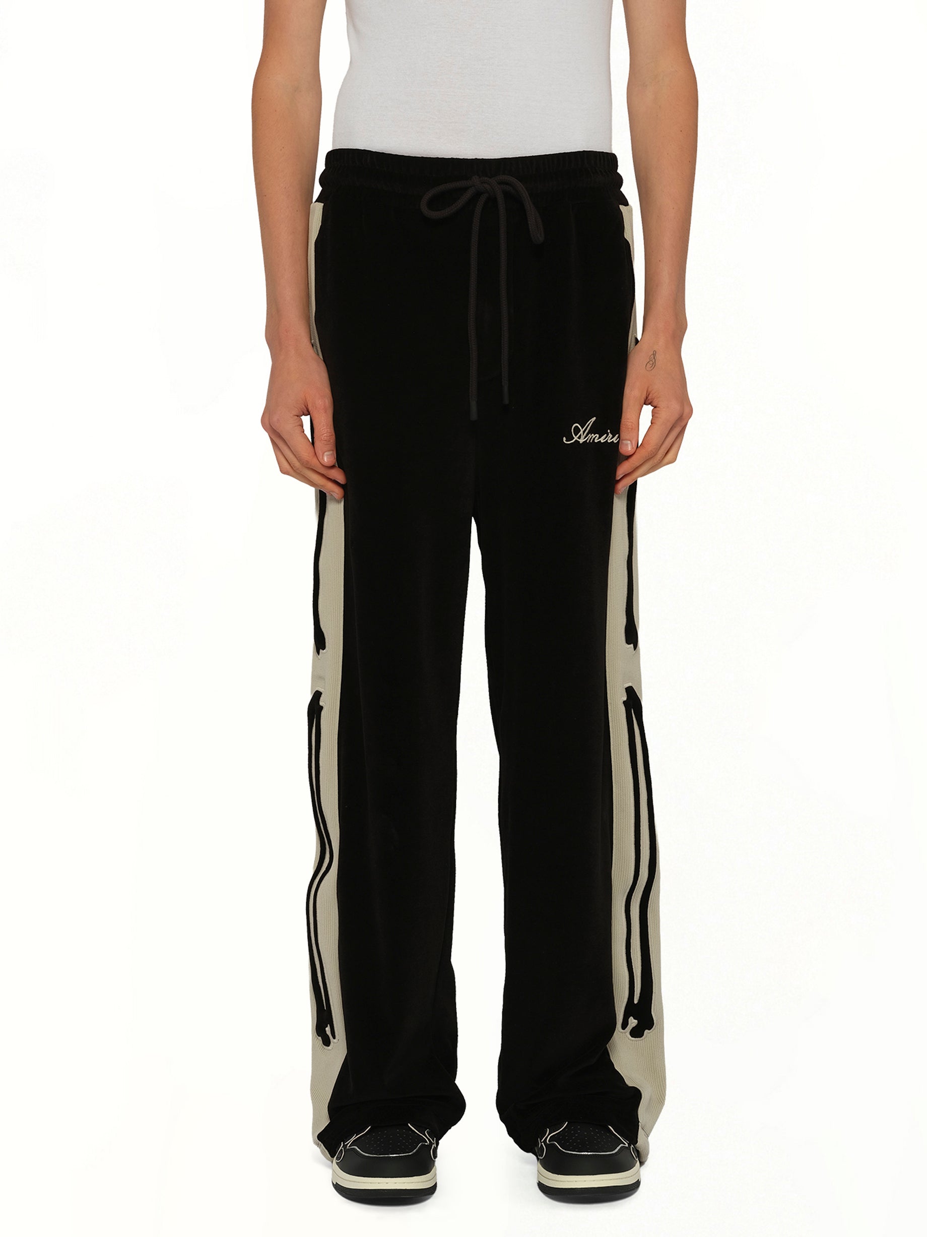 Image of a model wearing Pants. Product name - Bones Track Pant in Black colour by brand - AMIRI