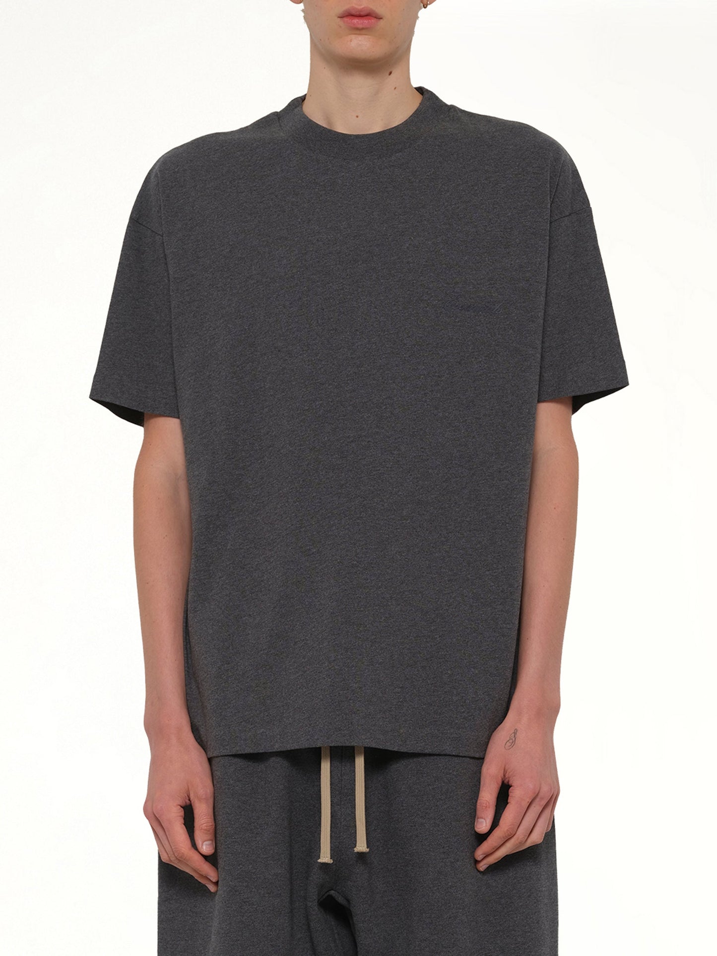 Image of a model wearing Tops. Product name - Classic Short Sleeve T-Shirt in Charcoal Heather colour by brand - FEAR OF GOD ESSENTIALS