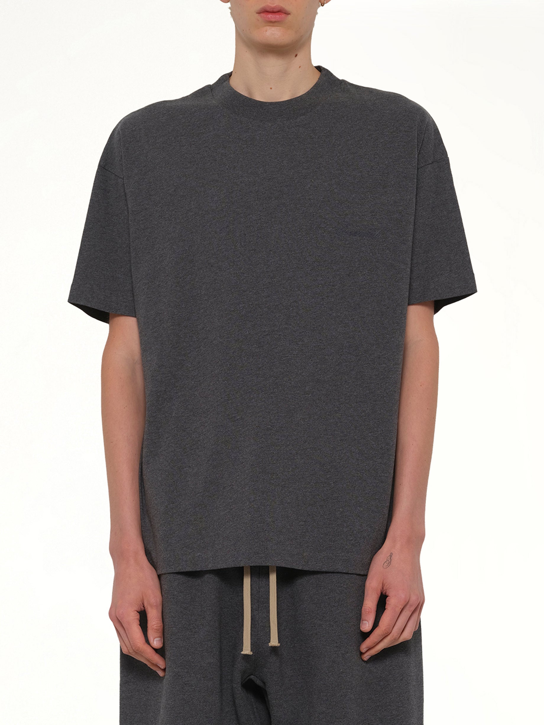 Image of a model wearing Tops. Product name - Classic Short Sleeve T-Shirt in Charcoal Heather colour by brand - FEAR OF GOD ESSENTIALS