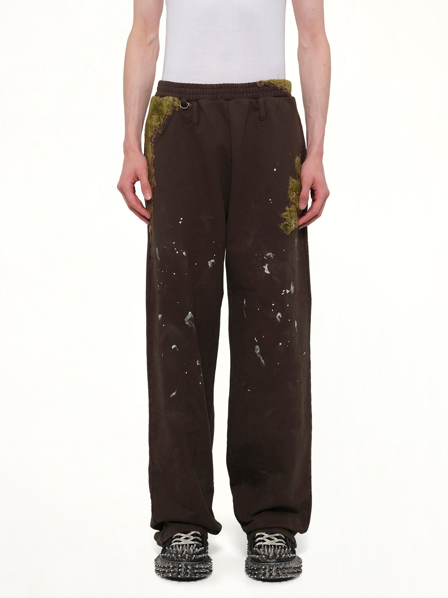 Image of a model wearing Pants. Product name - Moss-Grown Embroidery Sweat Pants in Brown colour by brand - DOUBLET