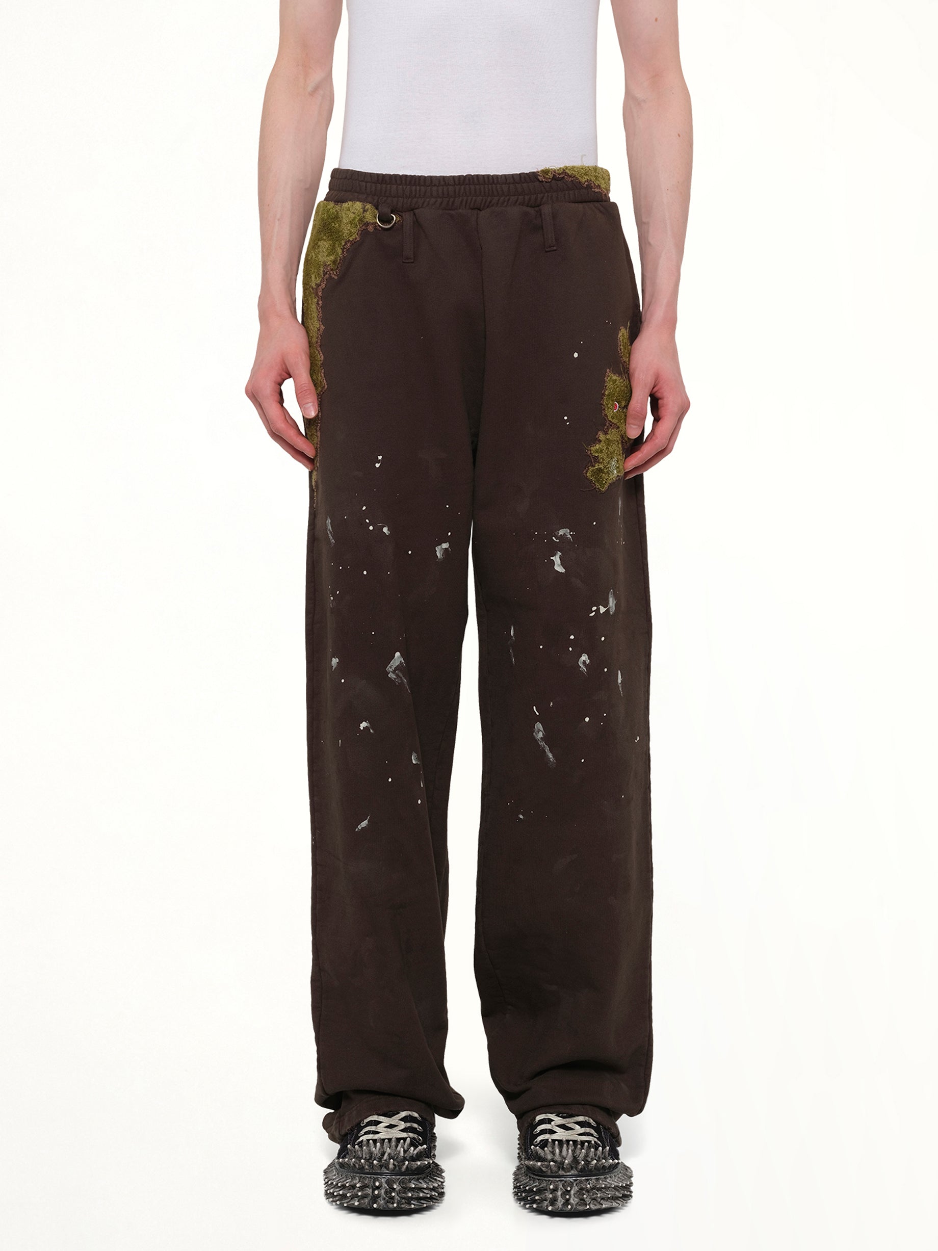 Image of a model wearing Pants. Product name - Moss-Grown Embroidery Sweat Pants in Brown colour by brand - DOUBLET