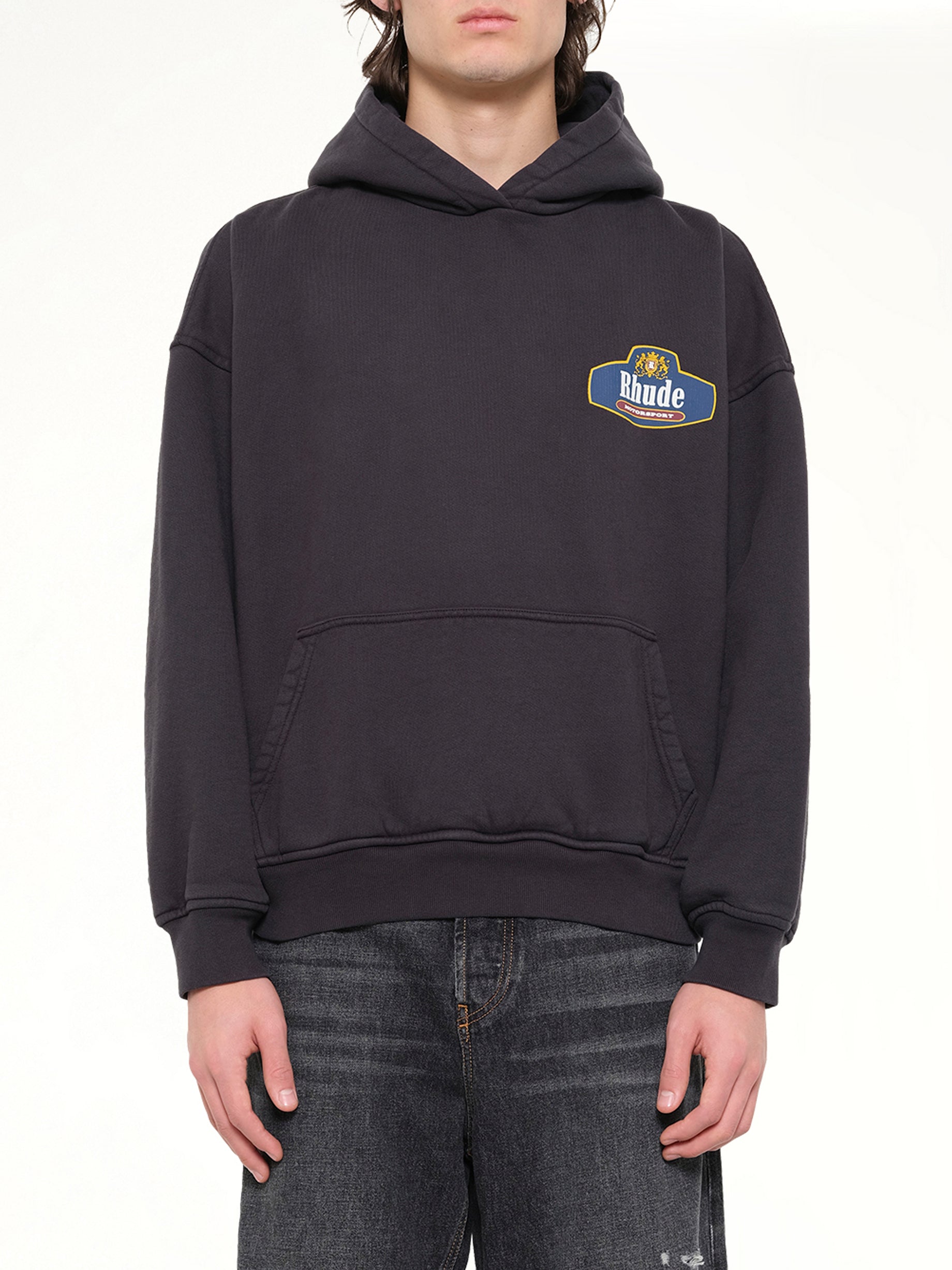 Image of a model wearing Outerwear. Product name - Racing Crest Hoodie in Black colour by brand - RHUDE