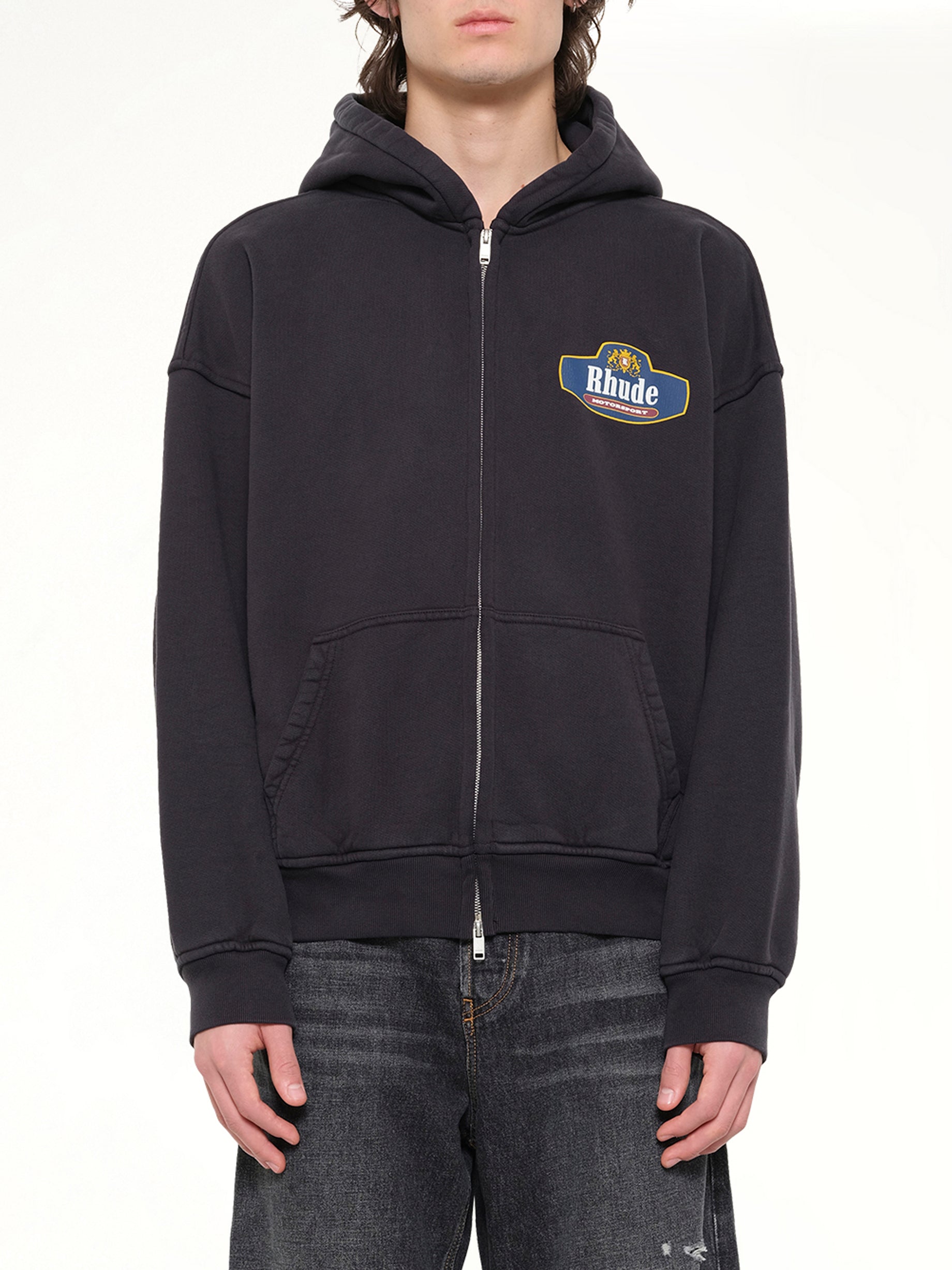 Image of a model wearing Outerwear. Product name - Racing Crest Zip-Up Hoodie in Black colour by brand - RHUDE