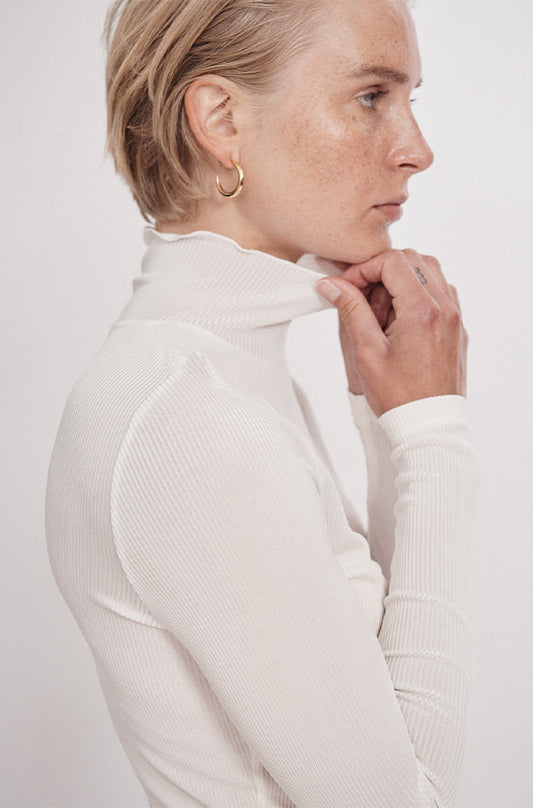 Image of a model wearing Tops. Product name - Ribbed Turtleneck White in White colour by brand - Silk Laundry