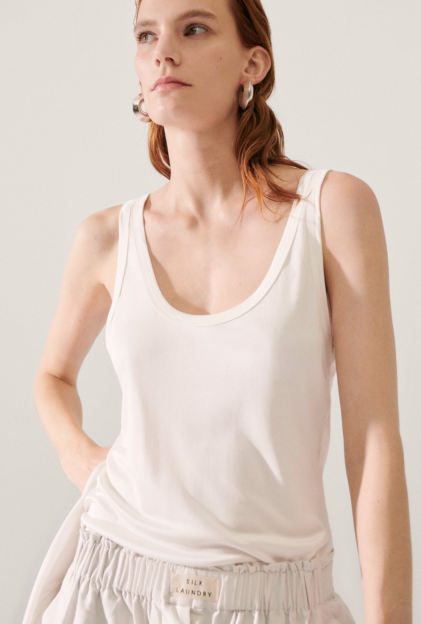 Image of a model wearing Tops. Product name - Jersey Scoop Tank White in White colour by brand - Silk Laundry