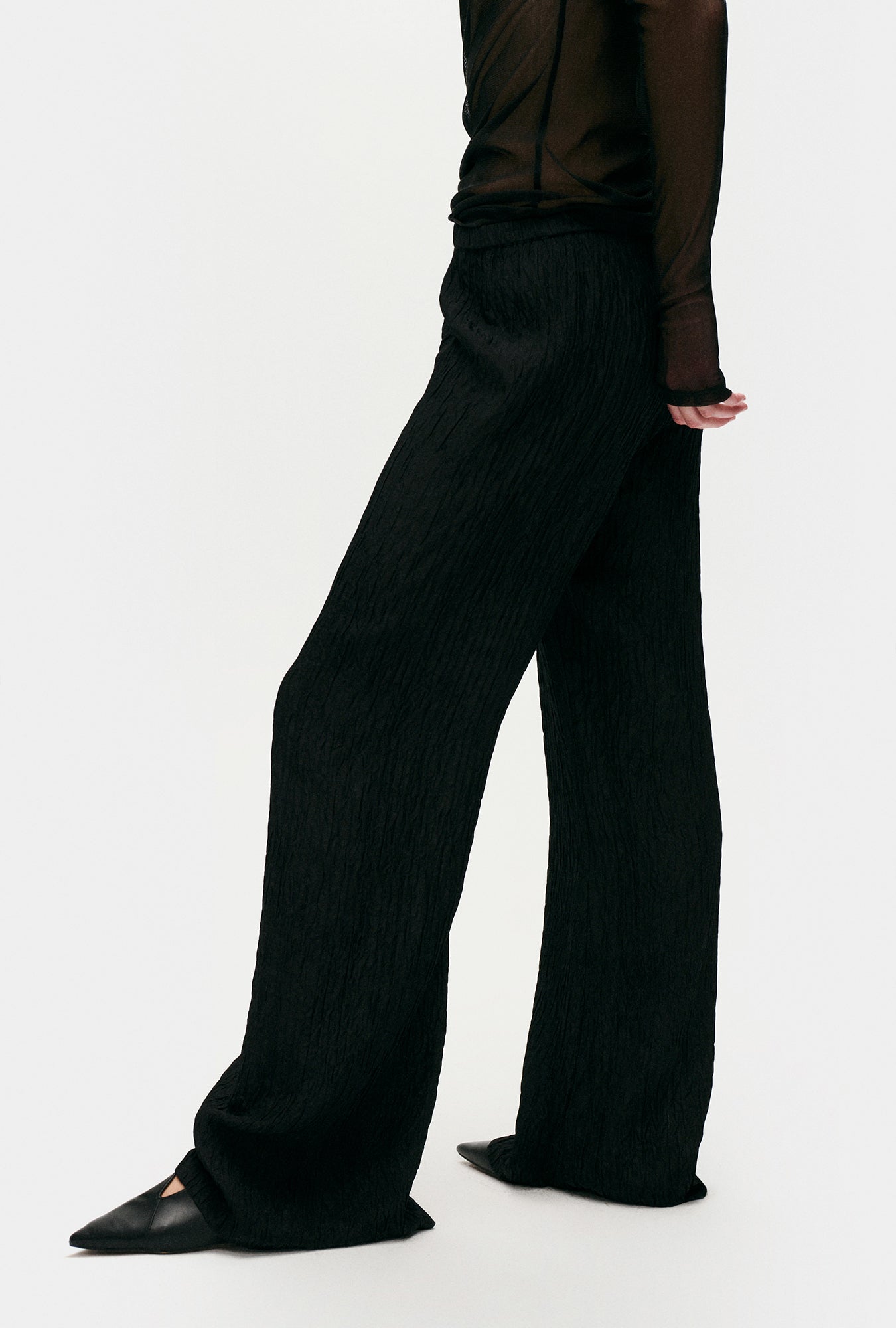 Image of a model wearing Pants. Product name - Crinkle Flare Pants Black in Black colour by brand - Silk Laundry