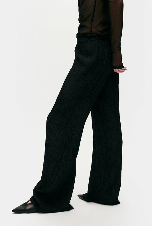 Image of a model wearing Pants. Product name - Crinkle Flare Pants Black in Black colour by brand - Silk Laundry