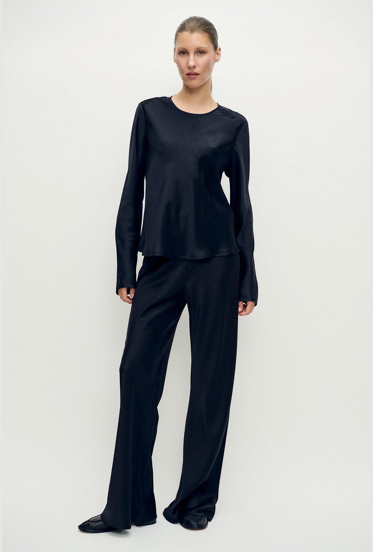 Image of a model wearing Tops. Product name - Long Sleeve Bias Top Black in Black colour by brand - Silk Laundry