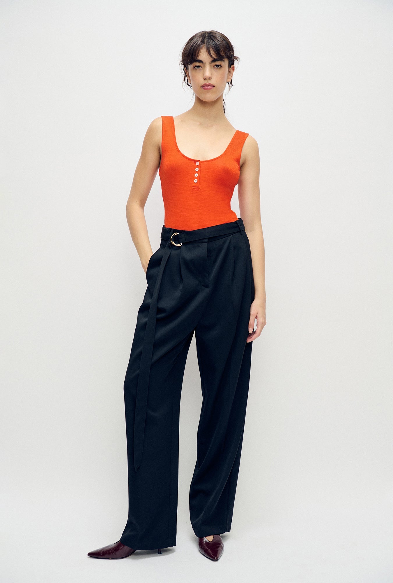 Image of a model wearing Tops. Product name - Merino Henley Tank Sunset in Sunset colour by brand - Silk Laundry