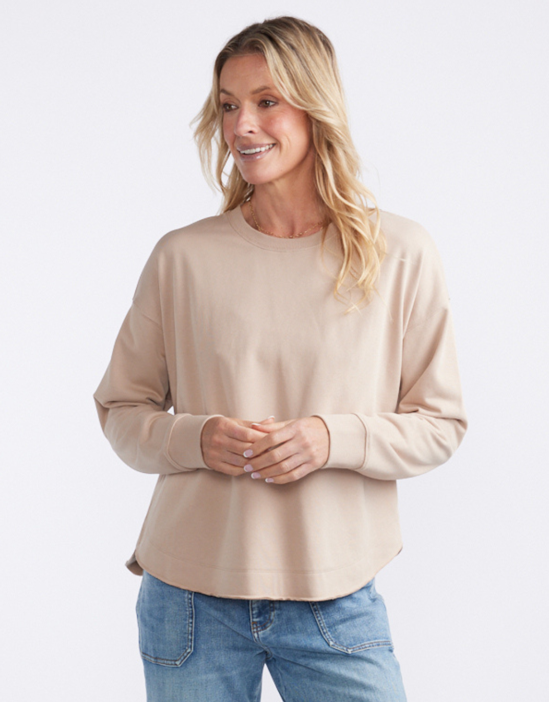 Image of a model wearing Outerwear. Product name - Staple Scoop Hem Sweat Latte in Latte colour by brand - White & Co.